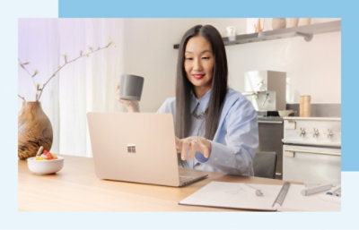 A woman with long hair in a blue shirt sitting at a desk with a laptop.