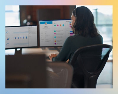 A person working at a desk with dual monitors displaying graphs and analytics.