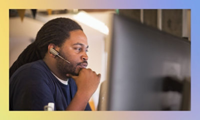 En mand med hovedtelefoner på, iført en blå skjorte, kigger på en computerskærm.