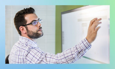 Person in a plaid shirt pointing at a whiteboard.