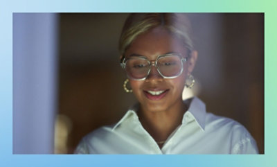 Person wearing a white shirt and earrings with a blurred face, standing indoors with a dimly lit background.
