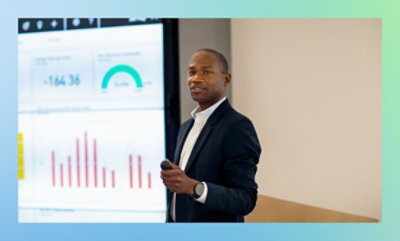 Person giving a presentation with a screen displaying graphs and charts in the background.