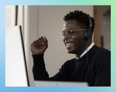 En mand med briller og et headset smiler, mens han kigger på en computerskærm. 