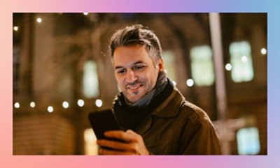Person holding a smartphone with string lights in the background during evening.