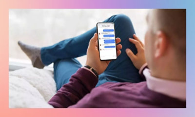 Eine Person sitzt mit übereinandergeschlagenen Beinen und schaut auf ein Smartphone mit einer Messaging-App auf dem Bildschirm.