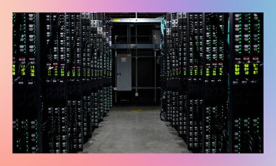 A corridor between rows of server racks in a data center with glowing lights on equipment.