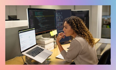 A person working at a desk with multiple computer screens displaying code and documents.