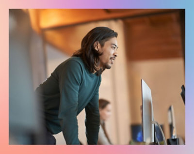 A man with long hair and a mustache looking at a computer screen.