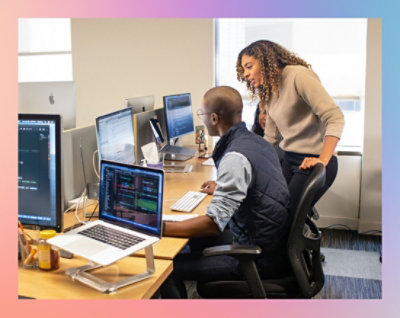 Dvě ženy spolupracují u stolu, na kterém je několik počítačových monitorů s kódem.