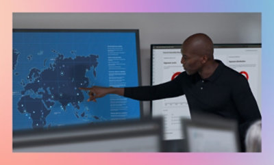 Person pointing at a digital world map on a large screen in a modern office setting.