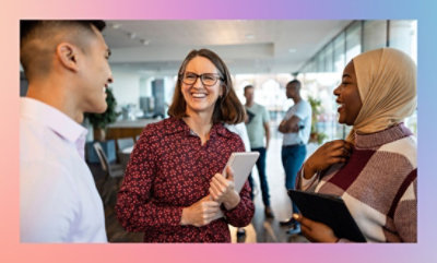 Three individuals engaged in a conversation in an office setting, with one person holding a tablet.