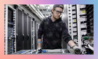 Person standing in a data center aisle between server racks, working on computer equipment.