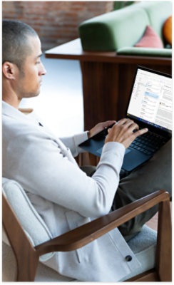A man sitting in a chair uses a laptop, viewing a split-screen display with an email inbox
