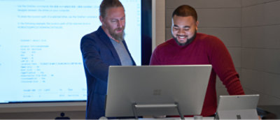 A man in a suit standing in front of a laptop.