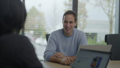 A person smiling and having a conversation with a coworker at a meeting table