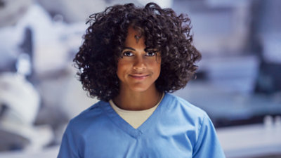 A person with curly hair wearing blue scrubs, standing in an indoor environment.