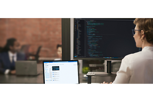 Una mujer trabaja en un portátil y un monitor de escritorio grande con código.