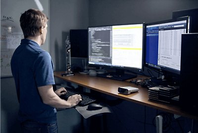 A person standing at their desk working across multiple monitors