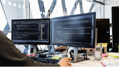 Two monitors at a desk displaying code.