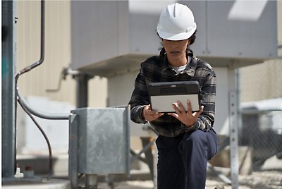 En person som bär en skyddshjälm böjer på knäna och använder en surfplatta