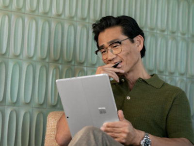 A person seated, working on the tablet mode of a Platinum Surface Pro 10.