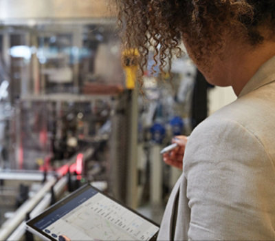 Eine Person mit lockigem Haar benutzt ein Tablet-Gerät in einer industriellen Umgebung und konzentriert sich auf einen Bildschirm 