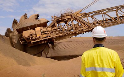 Pracownik obserwujący dużą maszynę kopiącą w piasku 