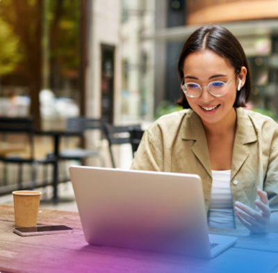 Smiling woman wearing earbuds uses a laptop at an outdoor cafe