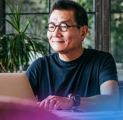 Smiling woman with glasses looks down while using a laptop