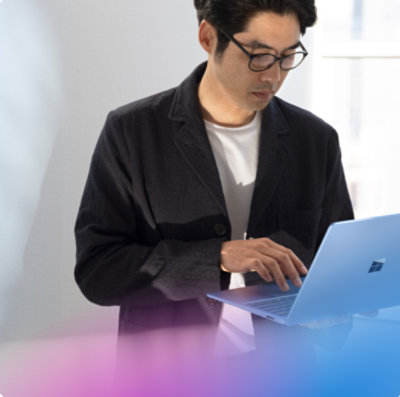 Man with glasses uses a Microsoft laptop while standing indoors