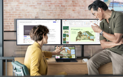 Two colleagues discuss a presentation; the woman, seated, points to a laptop screen