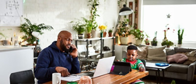 Una persona lavora a un portatile e parla al telefono seduta accanto a un bambino 