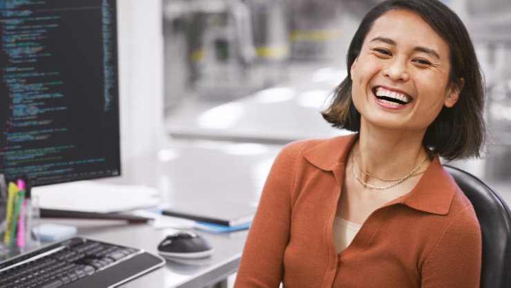 PC があるデスクで笑顔でこちらを向いている人物