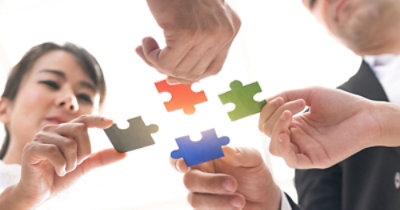 Četiri osobe sarađuju, pri čemu svaka drži i povezuje delove slagalice različitih boja.