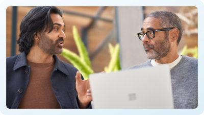A man with glasses and a beard talking with black jacket man. 