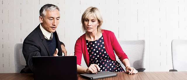 A man and woman sitting at a table looking at a laptop.