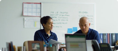 兩個人坐在白板前的桌子旁。