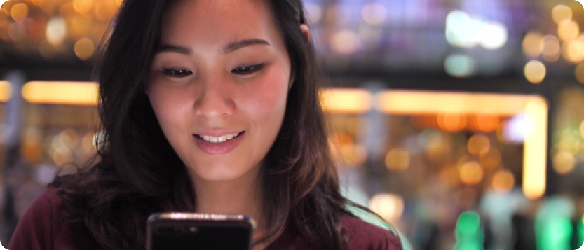 En ung asiatisk kvinna som tittar på sin mobiltelefon.