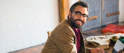 A man with glasses and a beard sitting at a table with a laptop.