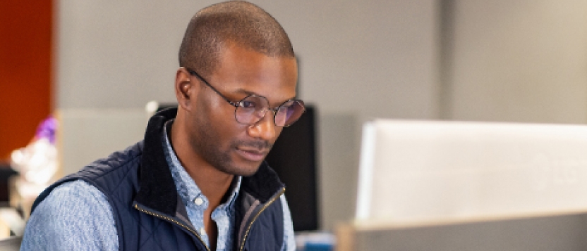 En man i glasögon arbetar på en dator.