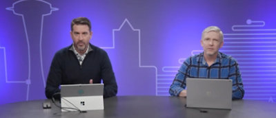 Two men sitting at a table with laptops in front of them.