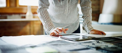 אדם בחולצה עם הדפס משתמש בטאבלט על שולחן עליו מפוזרים ניירות.