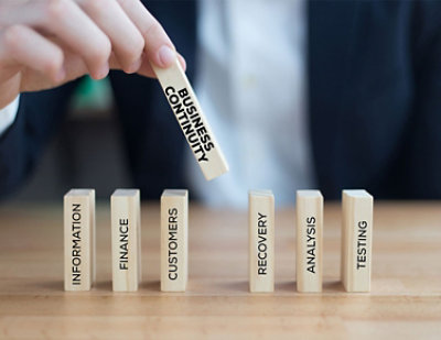 Hand holding wooden block over stack of dominoes with business related text.