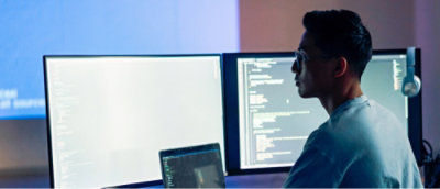 Person working with multiple computer monitors displaying code.