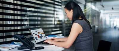 Kobieta w sukience bez rękawów jest skupiona przy laptopie na biurku, przeglądając aplikację kalendarza.