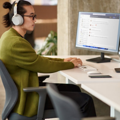 A man wearing headphones and sitting at a desk with two computers.