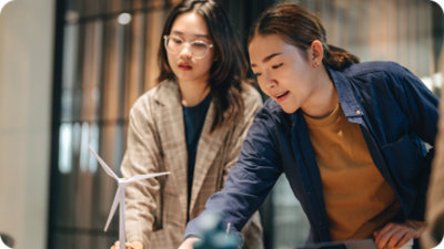 שני אנשים מתמקדים בדגם קטן של טורבינת רוח על שולחן בחלל עבודה מודרני.