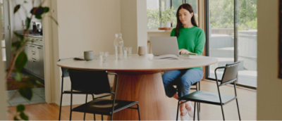 A woman in a green shirt sitting at a table using a laptop.