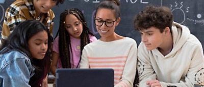 A woman wearing glasses and a white shirt is looking at a laptop with others nearby.
