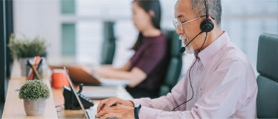 Un homme muni d’un casque travaille sur un ordinateur portable à un bureau, tourné vers l’avant. 